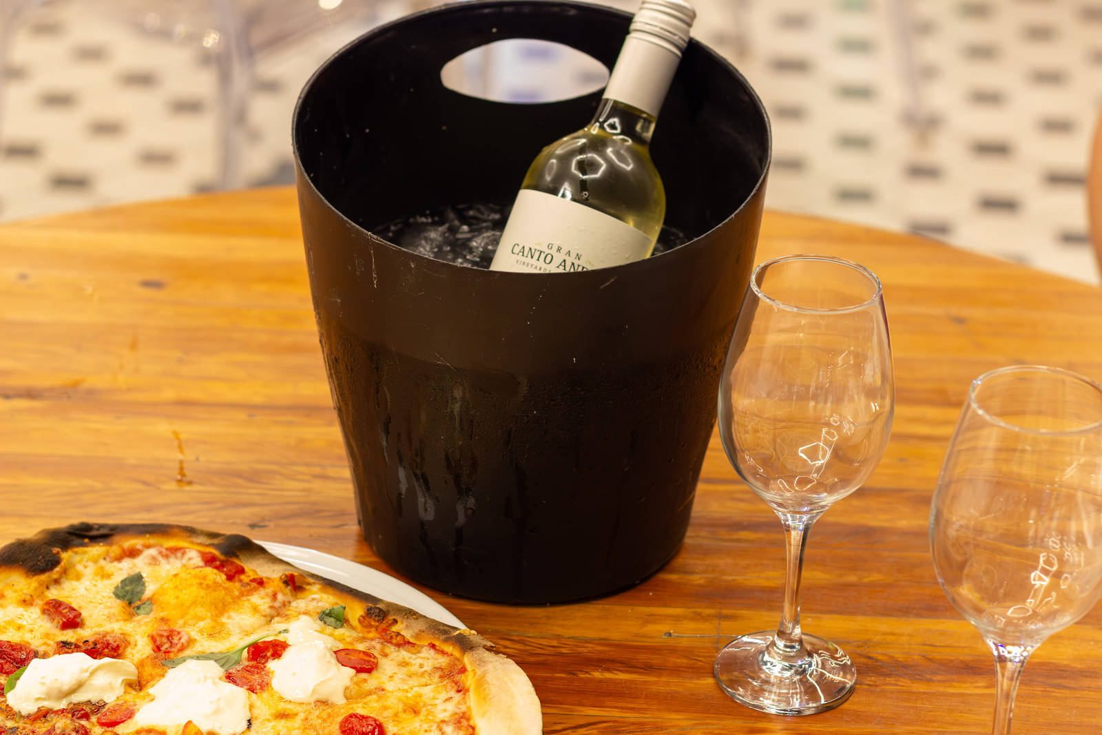 A bottle of white wine in an ice bucket beside Zona Sul pizza