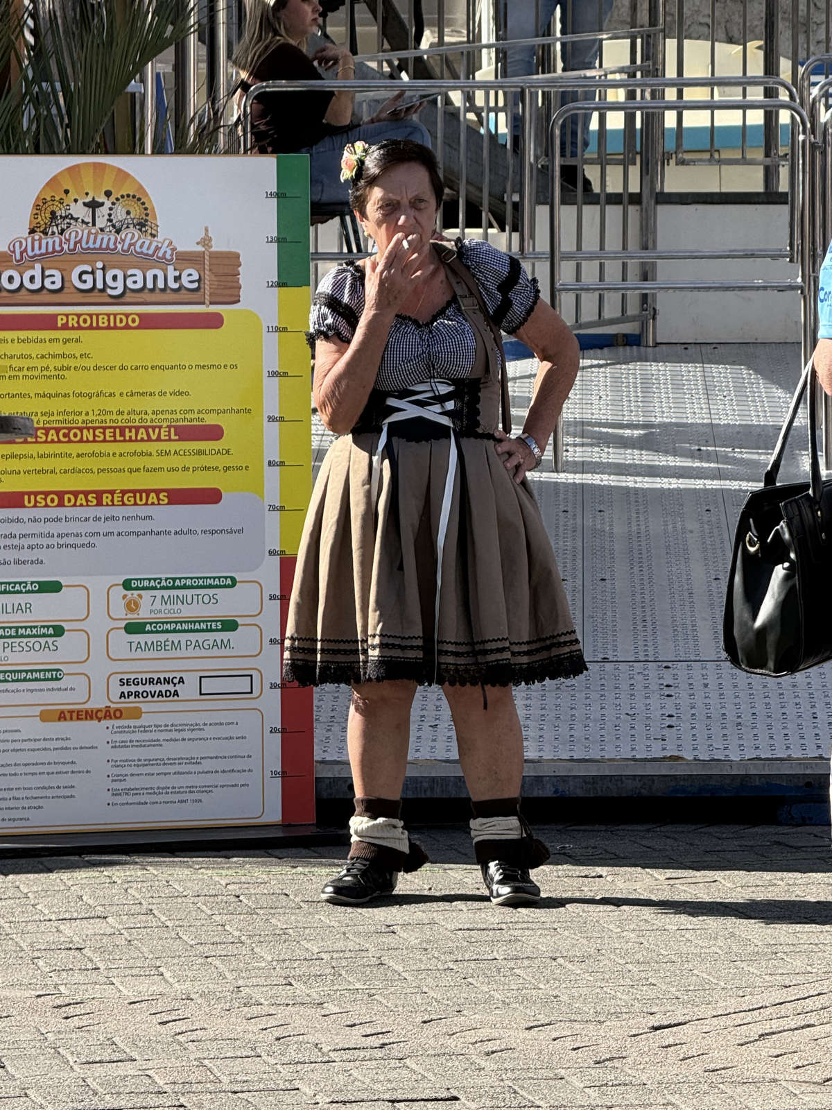 A visitor in traditional dress beside the Ferris wheel at Oktoberfest Blumenau